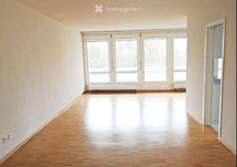 Empty room with wooden flooring, large windows, and white walls. No furniture or equipment present.