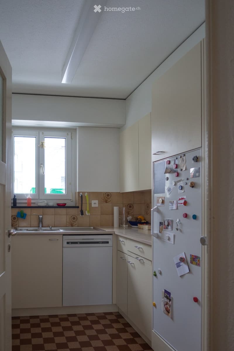A compact kitchen with a checkered floor, white cabinets, a stainless steel sink, a dishwasher, and a refrigerator adorned with notes and magnets.