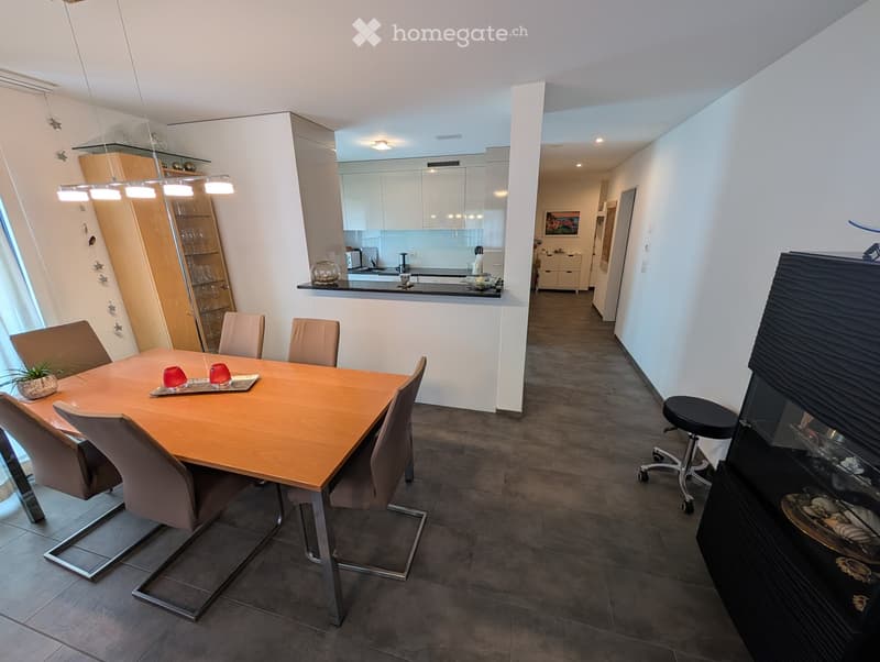 Modern dining area with a wooden dining table and chairs, a kitchen area with cabinets, a sink, and various appliances, and a small bar area with a stool.