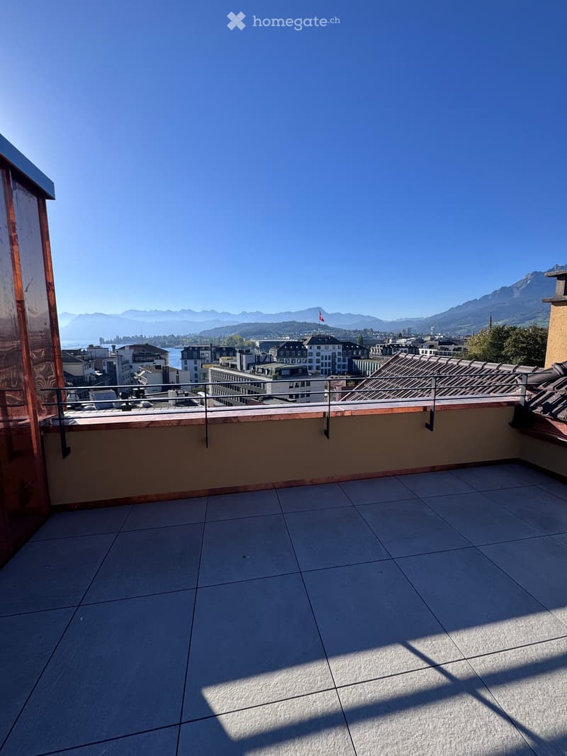 Roof terrace with tiled floor, metal railing, and panoramic city and mountain view.