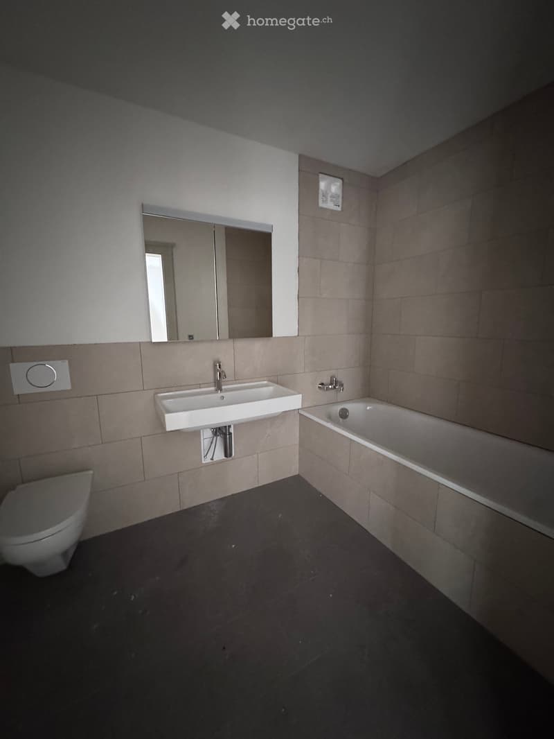 Modern bathroom with a white sink, bathtub, toilet, and large mirror. Beige tiled walls and dark tiled floor.