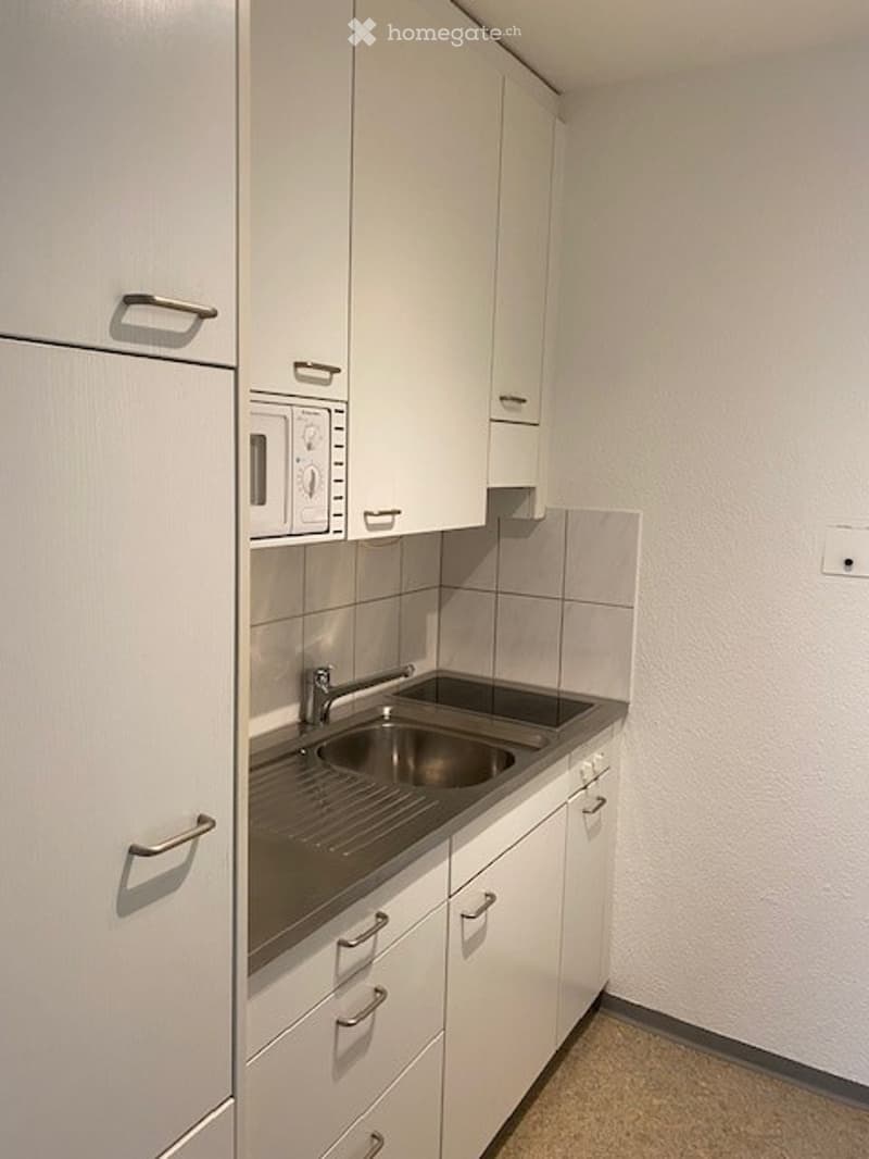 Modern kitchen with white cabinets, stainless steel sink, microwave, and tiled backsplash.