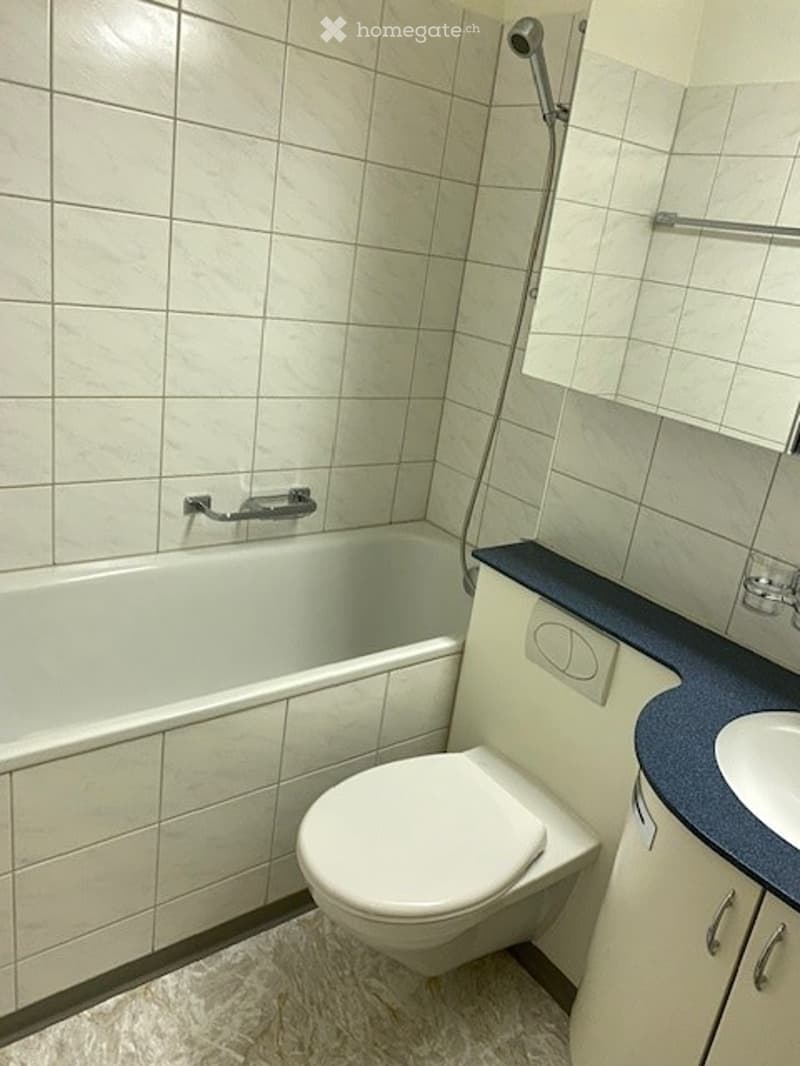 Modern bathroom with white tiled walls, a bathtub, toilet, sink, and a showerhead.