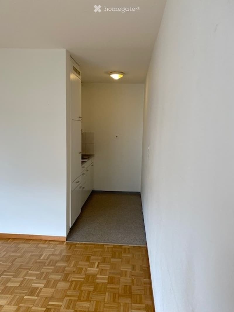 Empty room with wooden herringbone flooring, white walls, and a small built-in cabinet with drawers. No furniture or equipment present.
