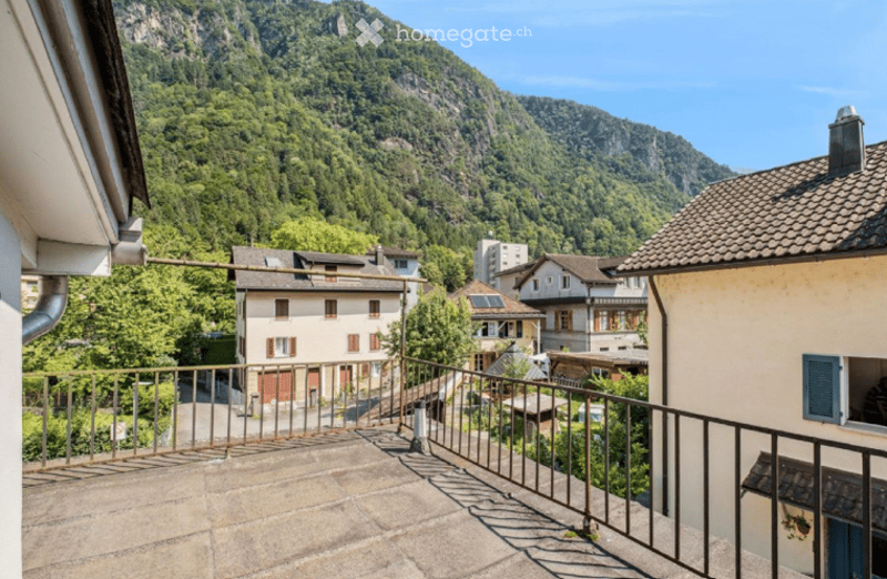 Balcony overlooking a scenic valley with houses and lush green hills in the background.
