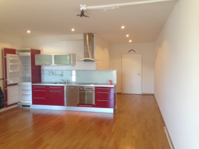 An empty modern kitchen with wooden floor, red cabinets, stainless steel appliances, a sink, and a gas stove.