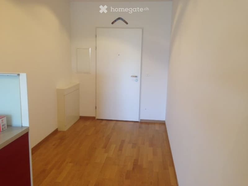 empty room with hardwood floor, white walls, small cabinet, entrance door, picture frame