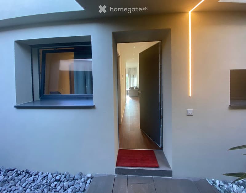 Modern hallway with wooden flooring, white walls, recessed lighting, and a red doormat leading to another room.