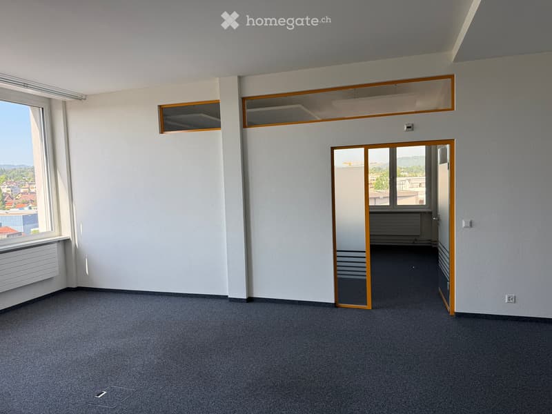 Empty room with grey carpet, white walls, large windows, and a glass door leading to another space.