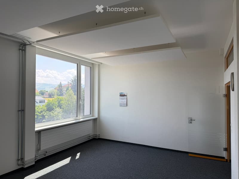 Empty room with white walls, large windows, radiator, and a calendar on the wall.