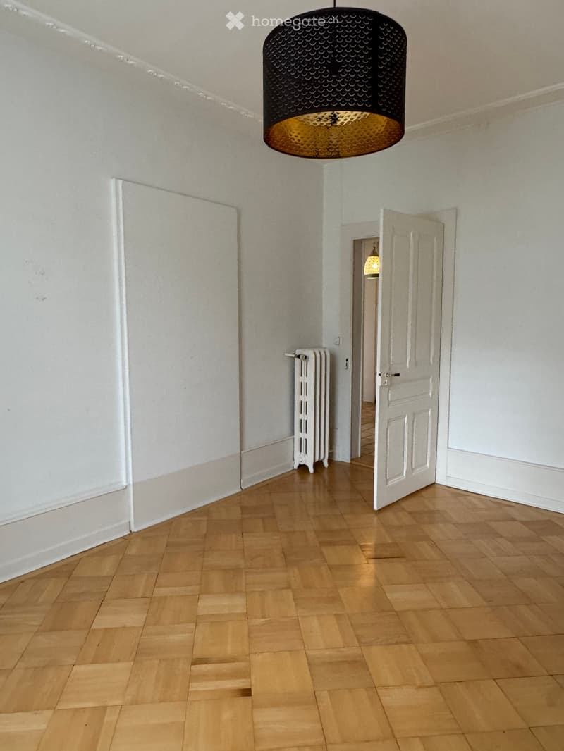 Empty hallway with wooden flooring, white walls, a radiator, and a hanging light fixture.