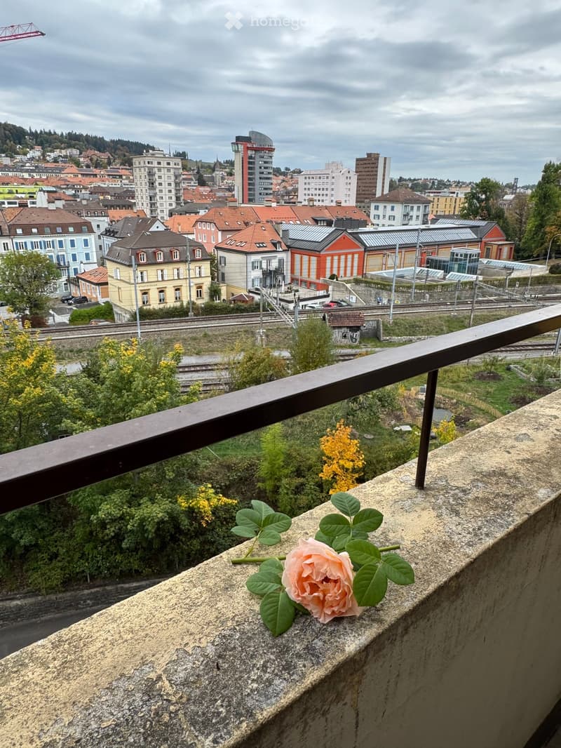 Balcony with a view of a cityscape, featuring a single rose placed on the ledge.