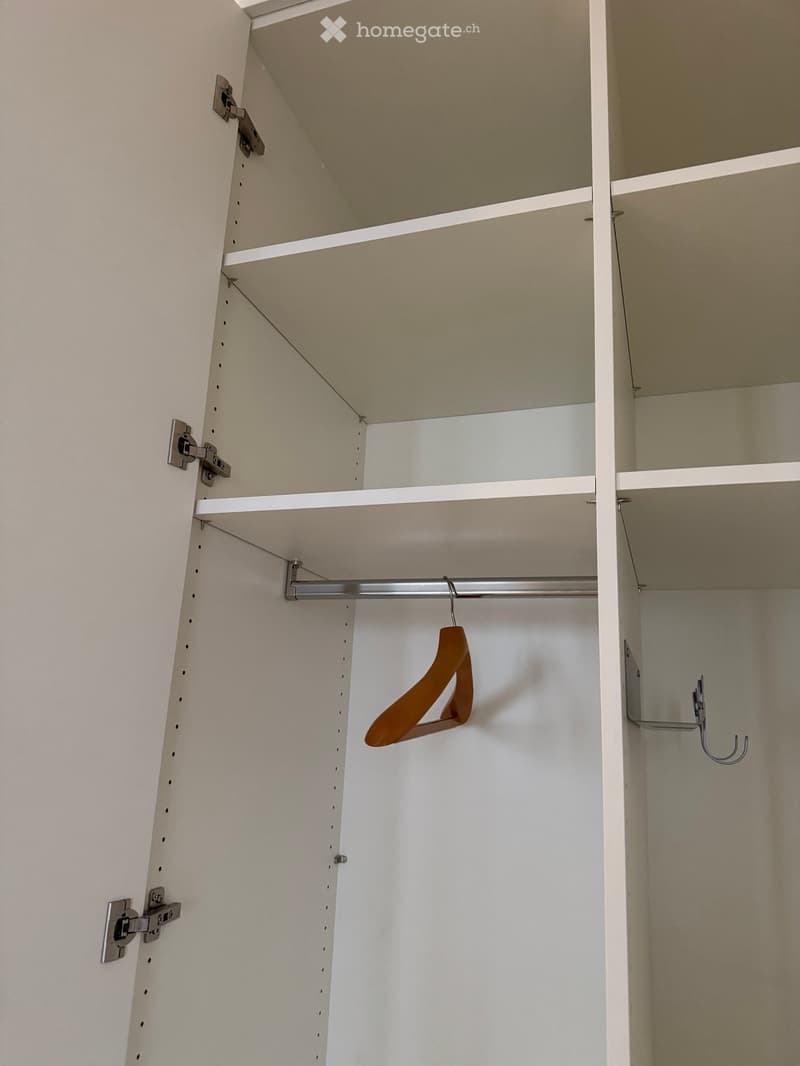 Empty closet with white walls, multiple shelves, and a single wooden hanger on a metal rod.