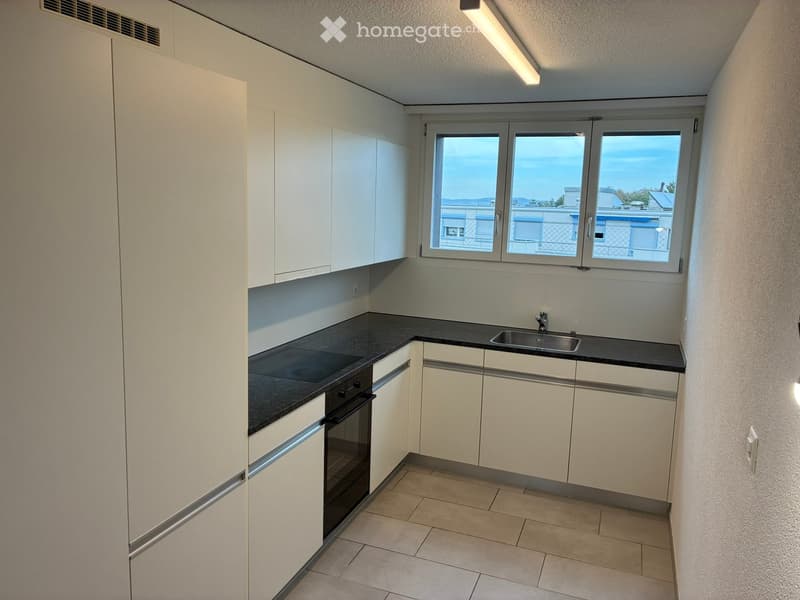 Modern kitchen with white cabinets, black countertops, and a sink, featuring large windows with a view of the surrounding area.