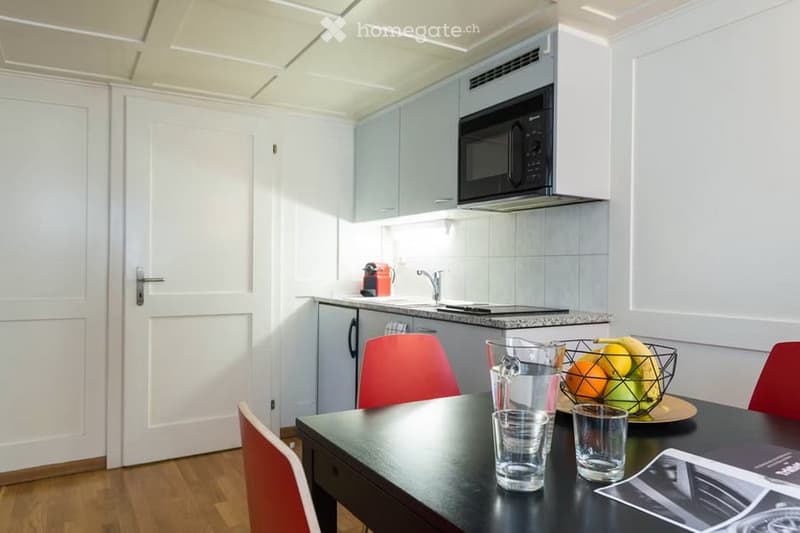 Modern kitchen with a black dining table, red chairs, microwave, and a fruit basket on the table.