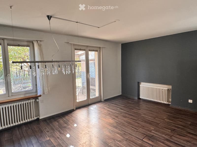 Empty room with wooden flooring, large windows, sliding glass doors, and modern lighting fixture.