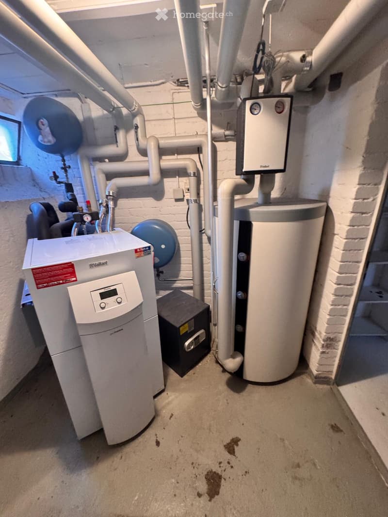 Utility room with water heater, boiler, control panel, and exposed pipes.