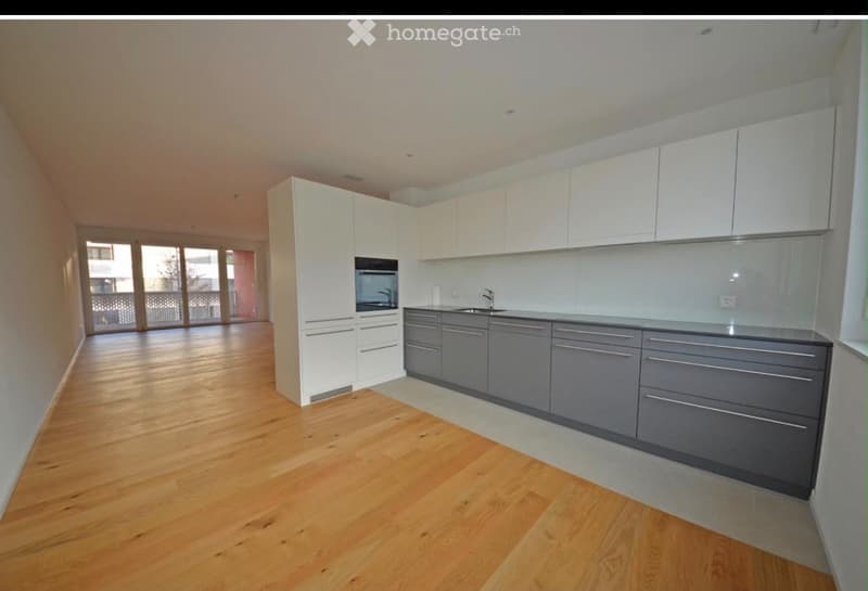 Modern kitchen with white and grey cabinets, wooden flooring, and large windows leading to a balcony.