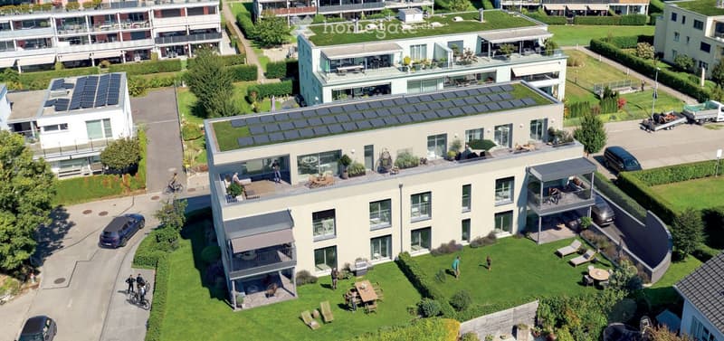 Aerial view of a modern residential complex with multiple buildings, green spaces, balconies, and solar panels on rooftops.