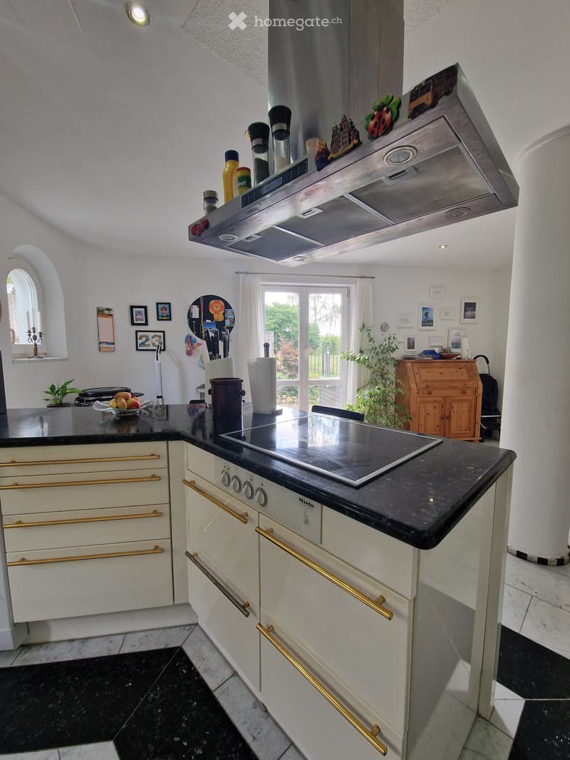 Modern kitchen with white cabinets, black countertops, induction stove, and various kitchen items on the counter.