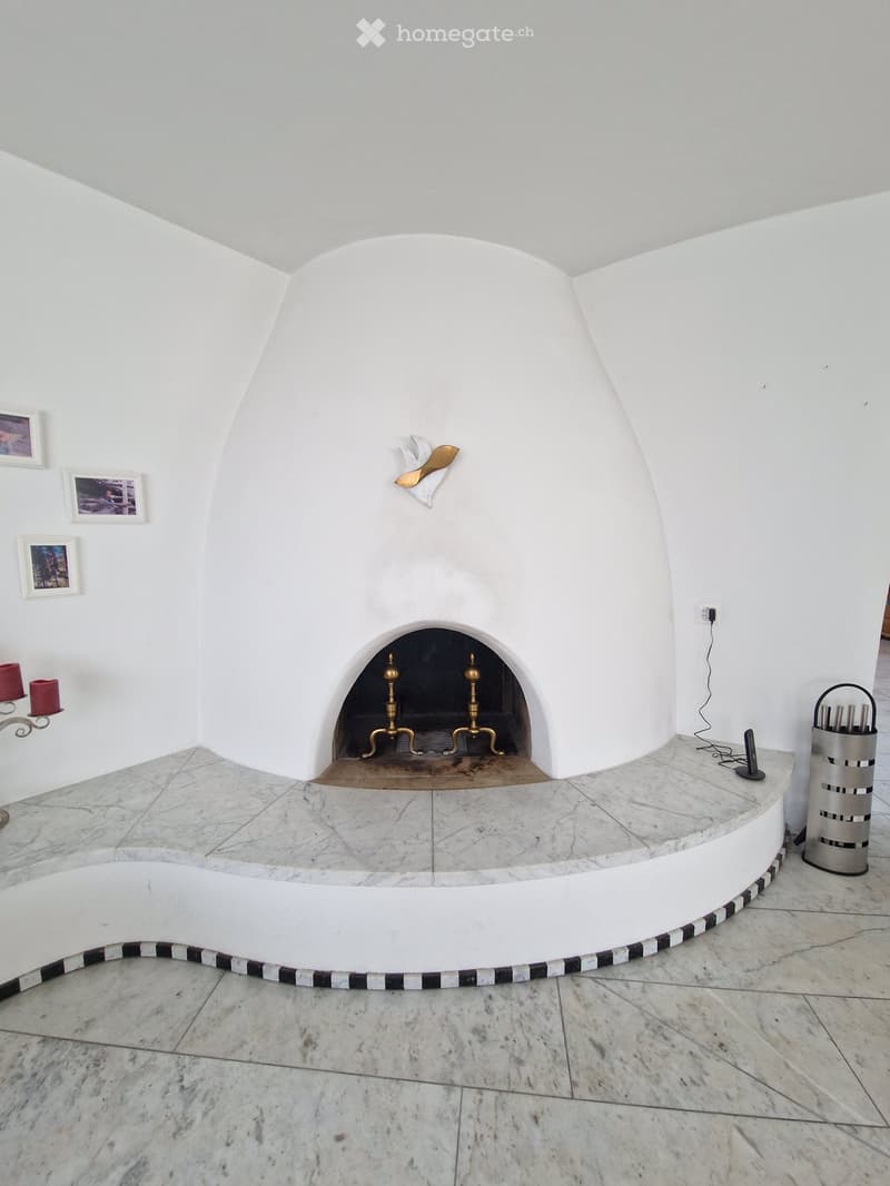 A modern, minimalist room with a prominent white arched fireplace, marble flooring, and decorative elements including candle holders and picture frames.