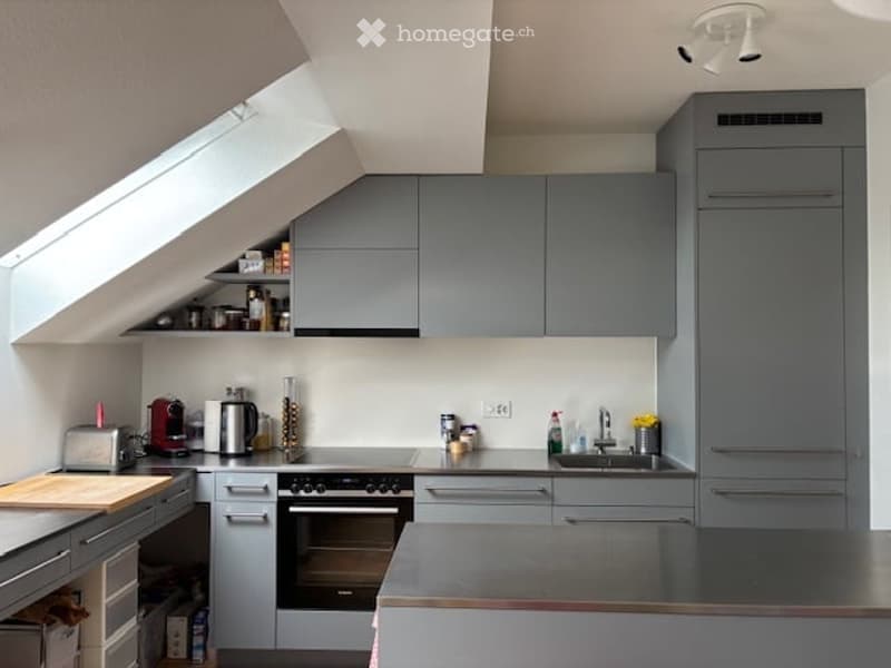 Modern kitchen with grey cabinets, stainless steel appliances, and a skylight window above the sink. The counter features a toaster, coffee maker, and cutting board.