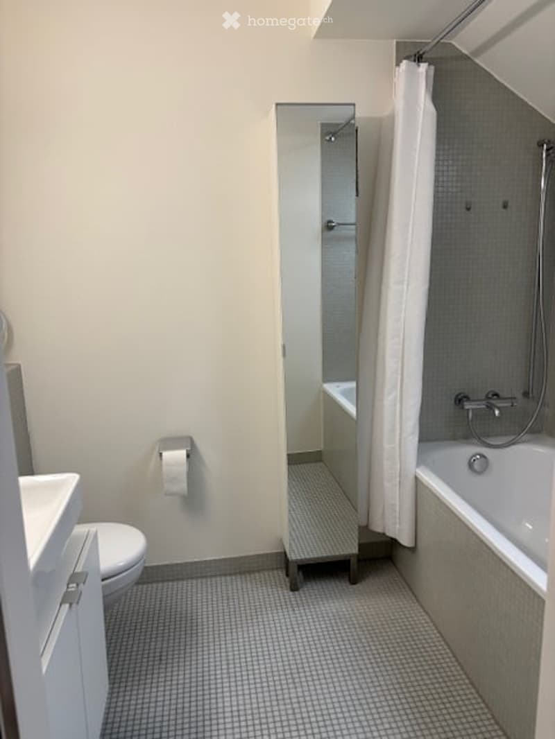 Modern bathroom with a toilet, sink, bathtub, mirror, and shower curtain. The space features a clean, minimalist design with a tiled floor and walls.