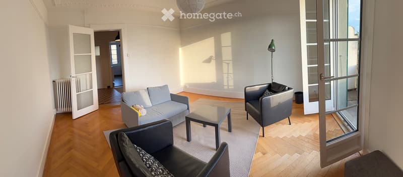 Bright living room with wooden flooring, large windows, and modern furniture including a sofa, coffee table, and armchairs.
