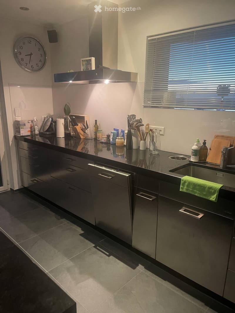 Modern kitchen with dark grey cabinets, stainless steel appliances, and a black countertop. Features a sink, faucet, dishwasher, and various kitchen utensils.
