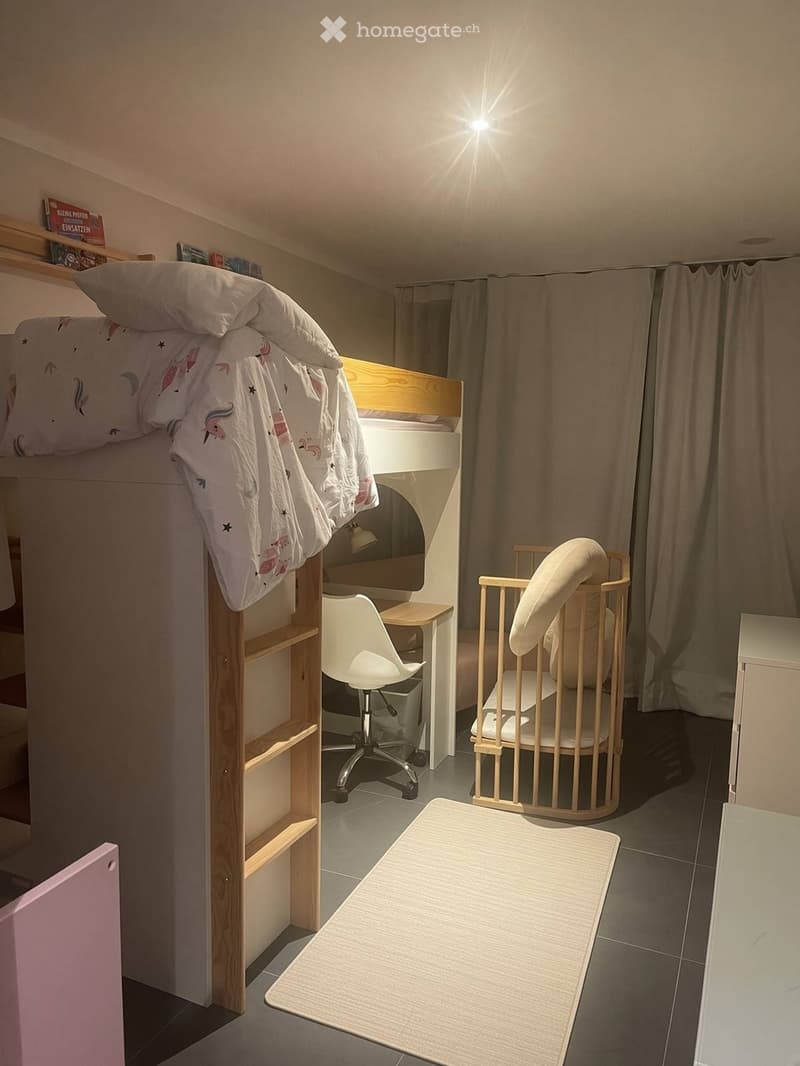 Cozy room with a lofted bed, desk, chair, and shelf. Features a small round chair and a white rug on the floor.
