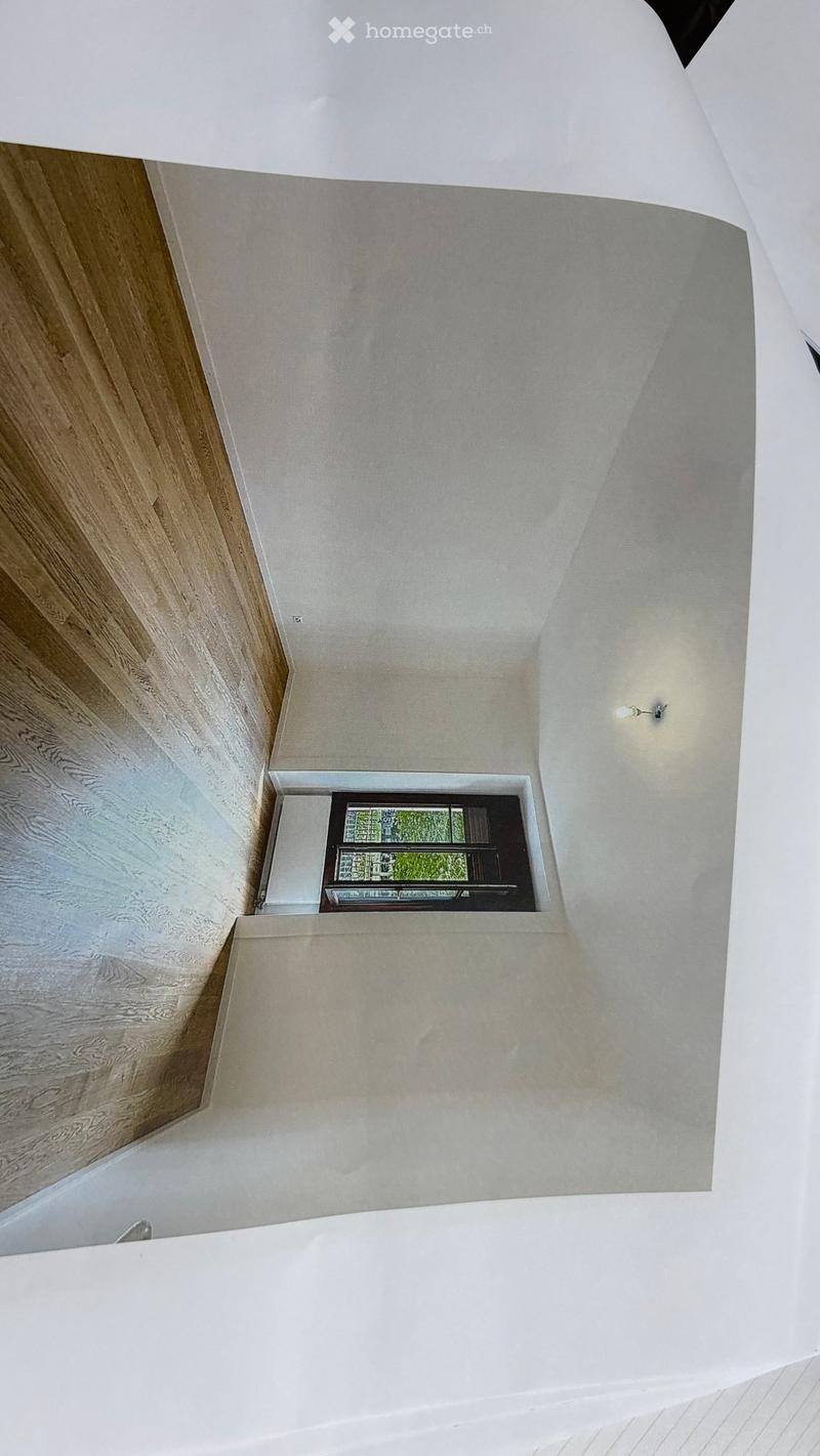 An empty room with light-colored walls, wooden flooring, and a small window with a decorative glass design. The ceiling has recessed lighting and a modern, minimalist design.