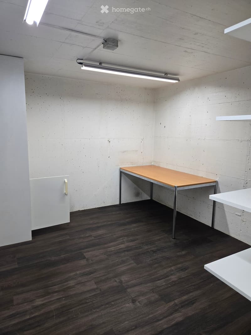 Minimalist room with dark wooden flooring, white concrete walls, and a single wooden table with metal legs. A white cabinet is visible on the left side.