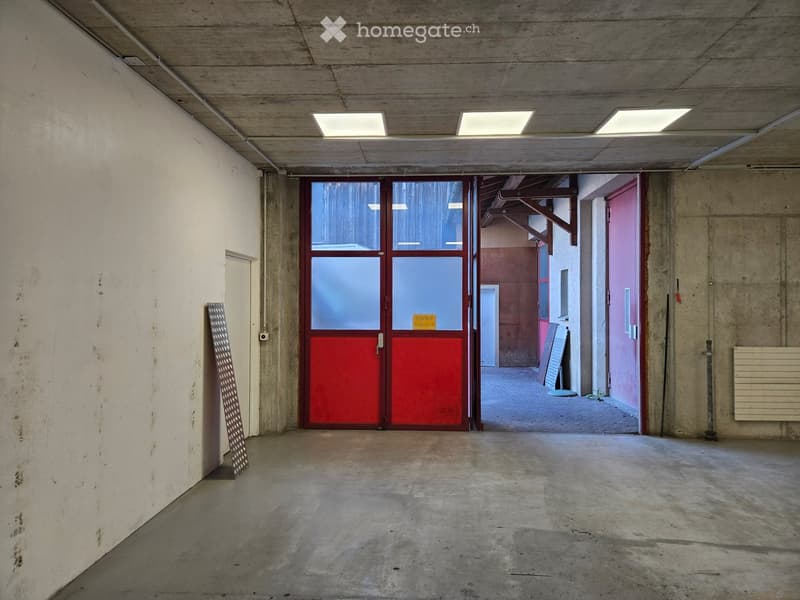 Empty concrete corridor with a large red double door, white walls, and a metal staircase on the left side.