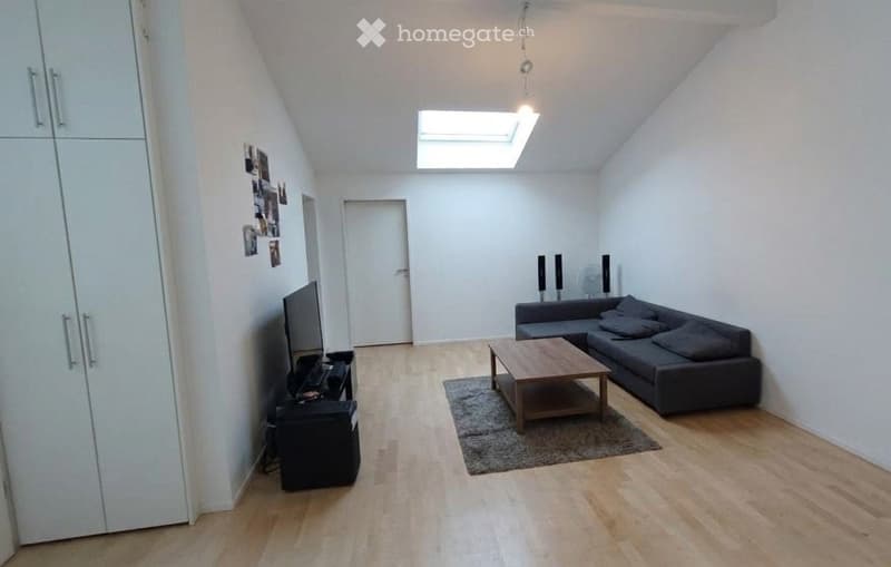 Modern living room with wooden flooring, grey sectional sofa, coffee table, TV, and a large skylight providing natural light.