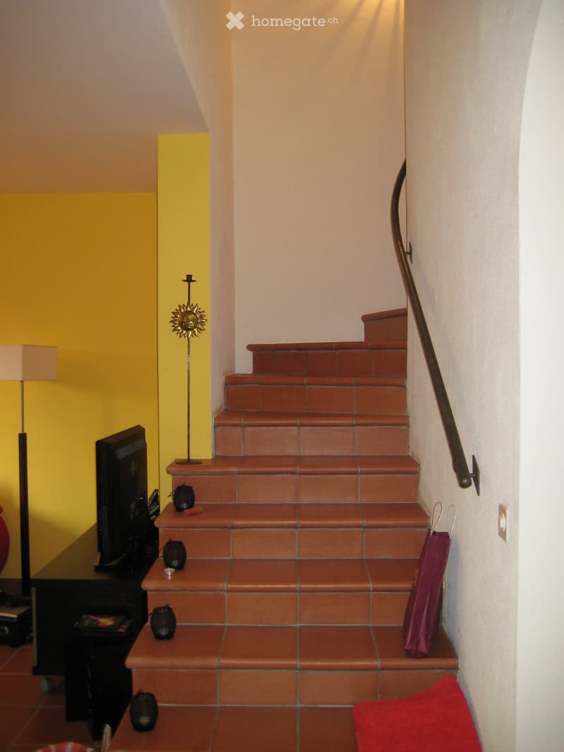 Staircase with terracotta tiles, metal railing, and decorative items on the steps and surrounding area.