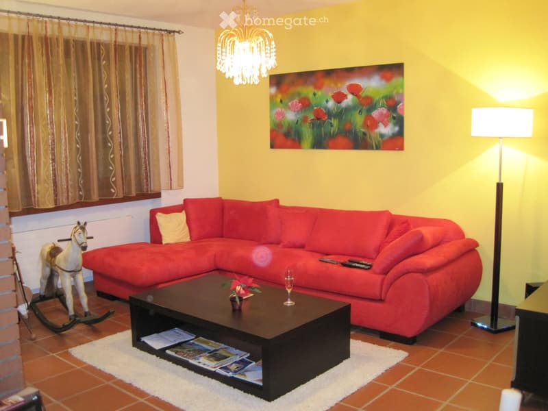 Bright living room with red sectional sofa, black coffee table, floor lamp, chandelier, and decorative painting.