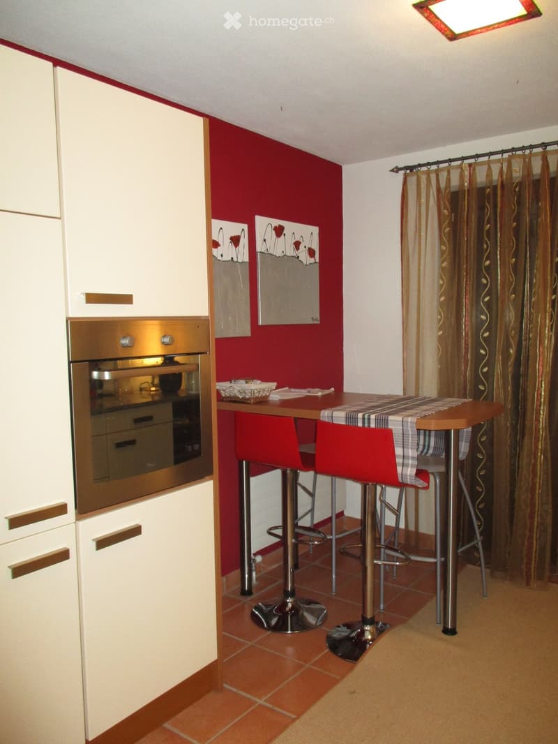 Modern kitchen with white cabinets, a built-in oven, a small dining table with two red stools, and decorative artwork on the wall.