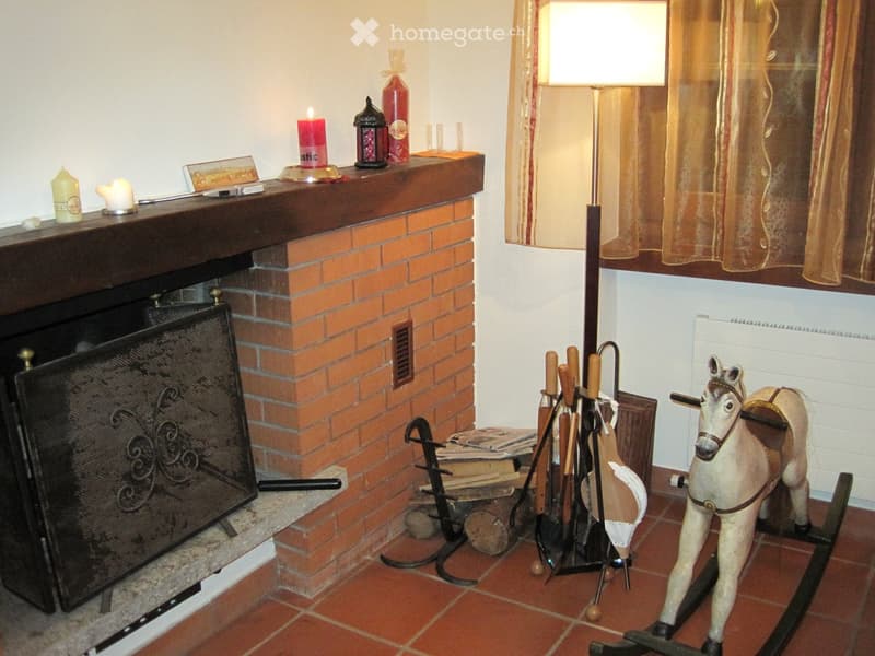 Living room with a brick fireplace, candles on the mantel, a rocking horse toy, a floor lamp, and fireplace tools.