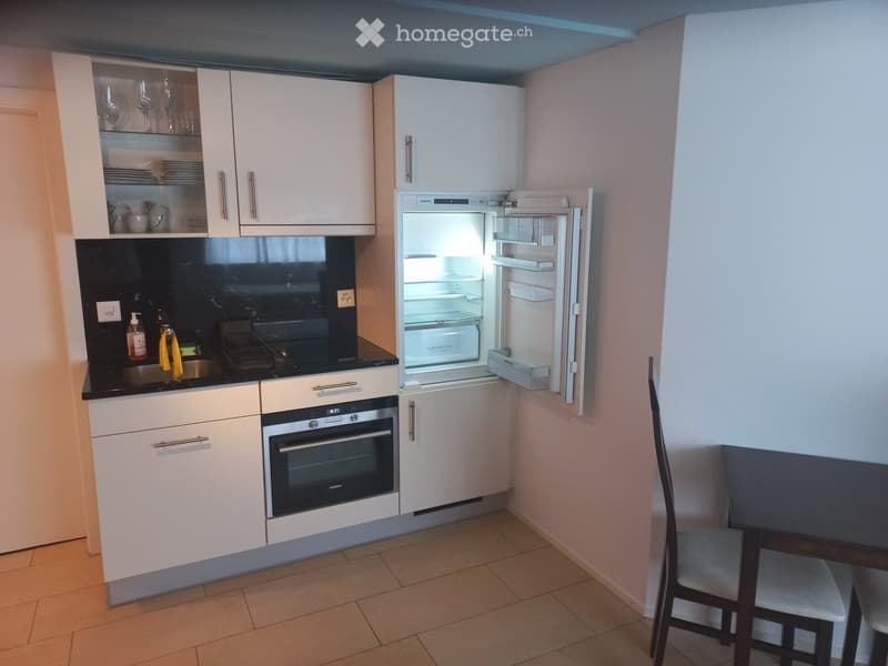 Modern kitchen with white cabinets, stainless steel appliances, and a small dining area with a table and chairs.