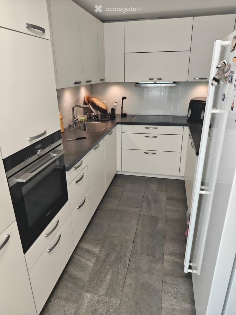 Modern kitchen with white cabinets, stainless steel appliances, and a dark countertop. Features include an oven, refrigerator, sink, and various kitchen utensils.