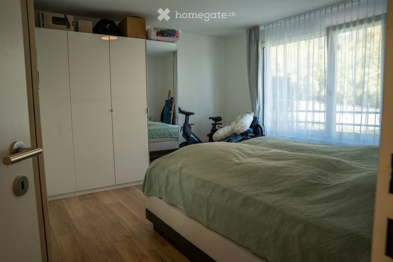 Bedroom with a double bed, green duvet, large wardrobe, mirror, and exercise bike near the window.