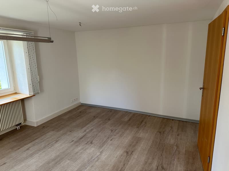 Empty room with wooden flooring, white walls, a window with blinds, a radiator, and a wooden door.