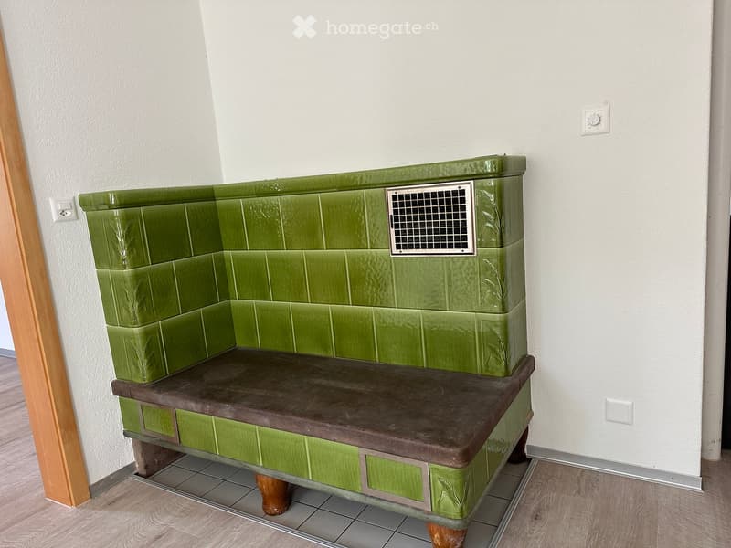 Green tiled bench with a wooden seat and decorative carvings, placed against a white wall with a vent.