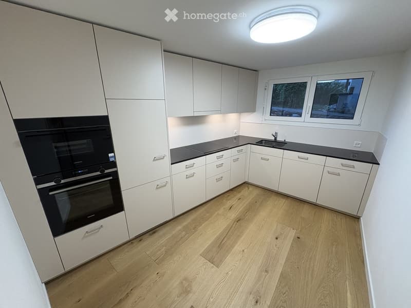 Modern kitchen with white cabinets, wooden flooring, and stainless steel appliances including an oven and sink.