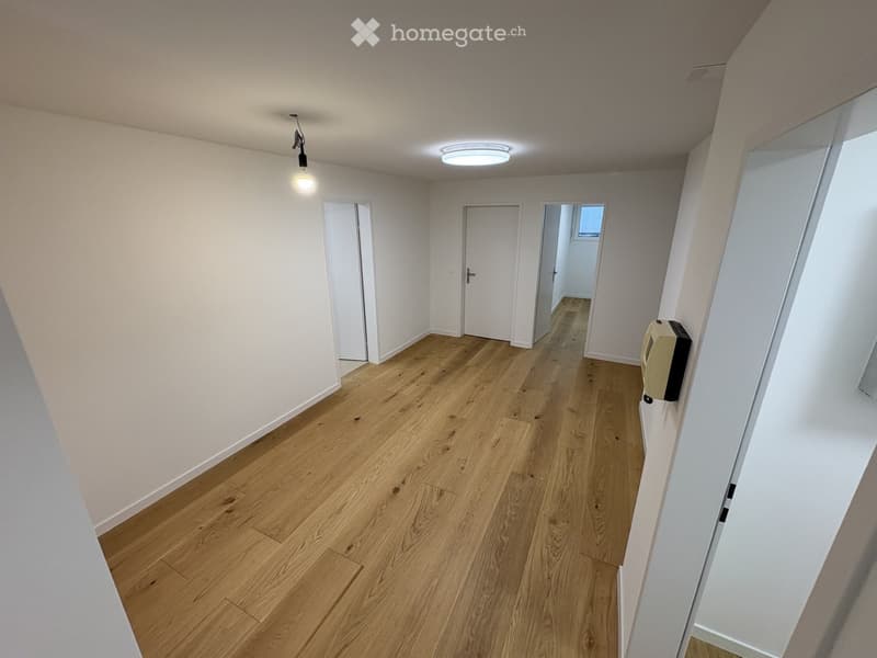 Empty hallway with wooden flooring, white walls, and several doors leading to other rooms.