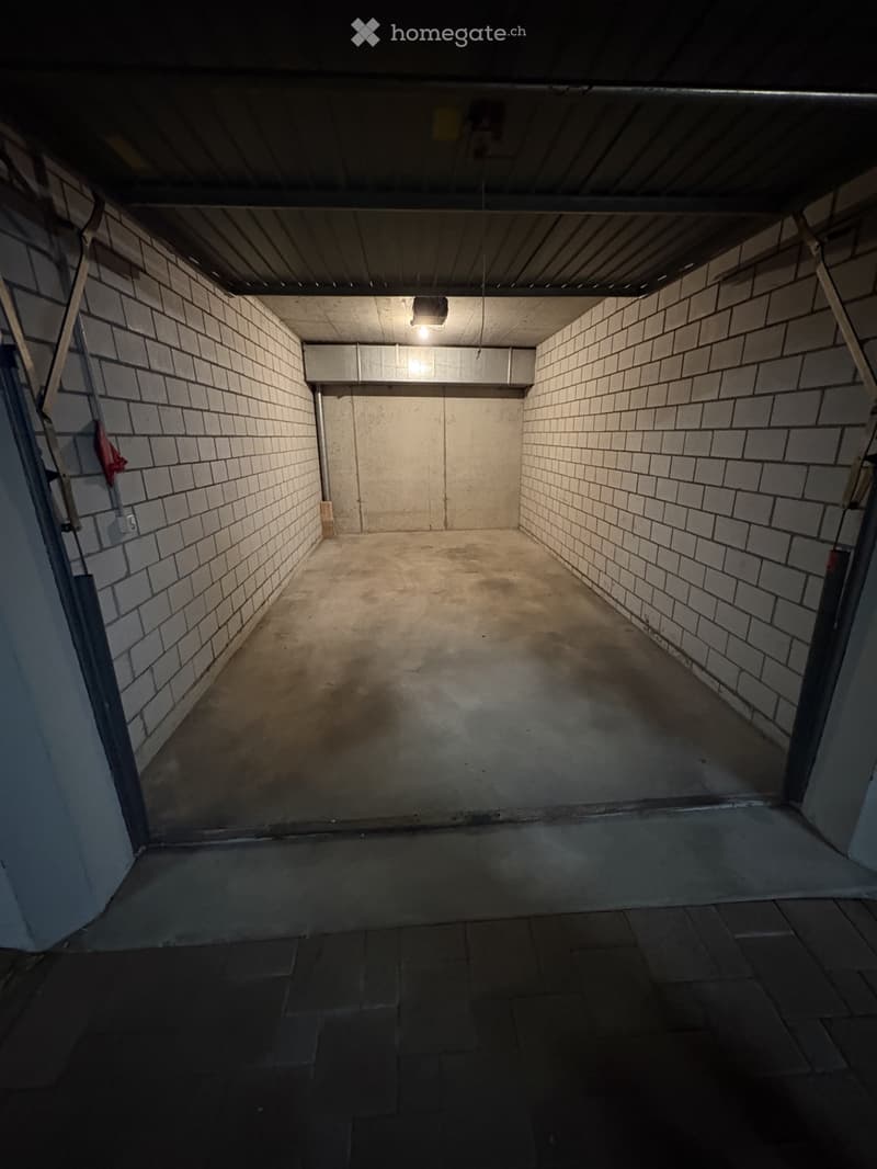Empty underground garage with concrete floor, brick walls, and metal ceiling. No furniture or equipment present.