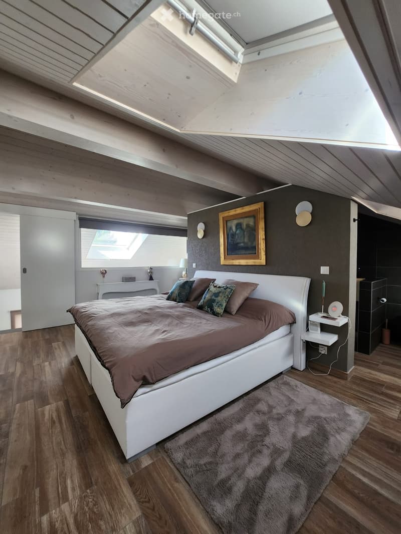 Modern attic bedroom with wooden floors, white bed, nightstand, table lamp, and artwork on the wall.