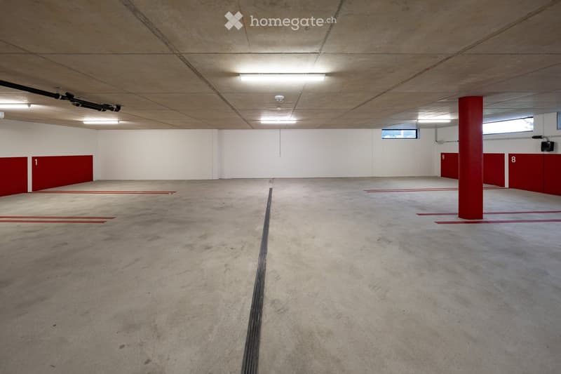 Empty underground parking area with concrete floors, white walls, red pillars, and numbered parking spots.