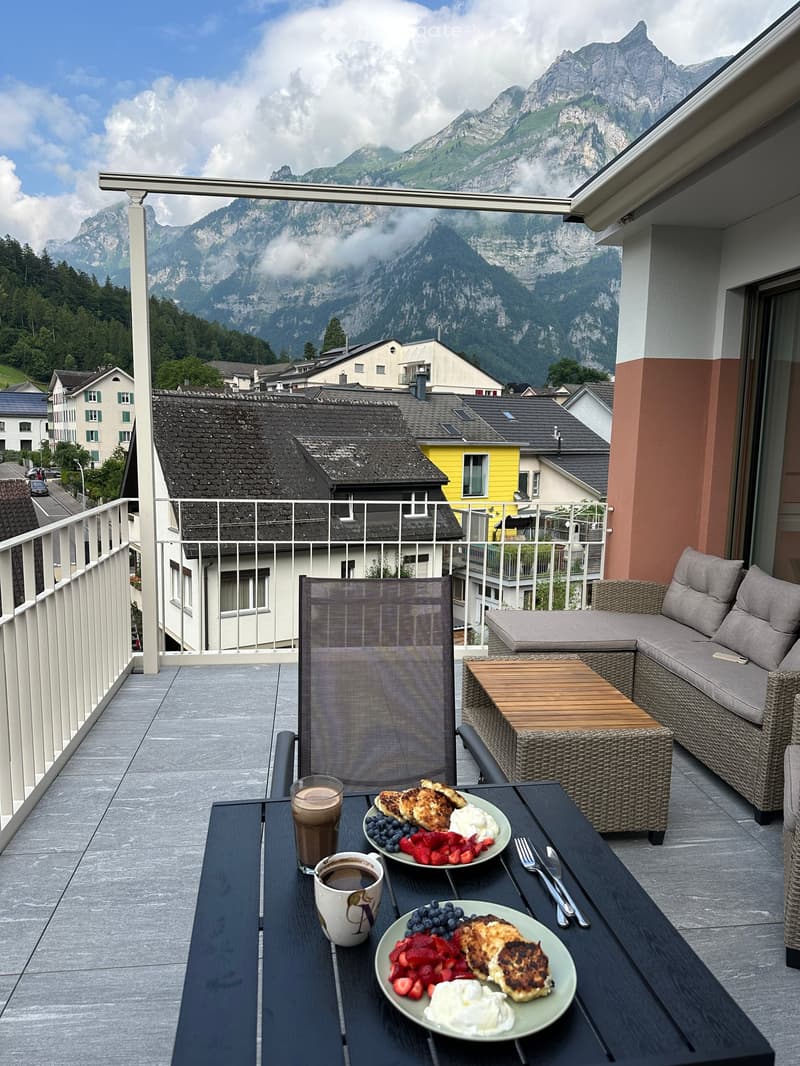 Balcony with a scenic mountain view, featuring a table set with breakfast items, a sofa, and a chair.