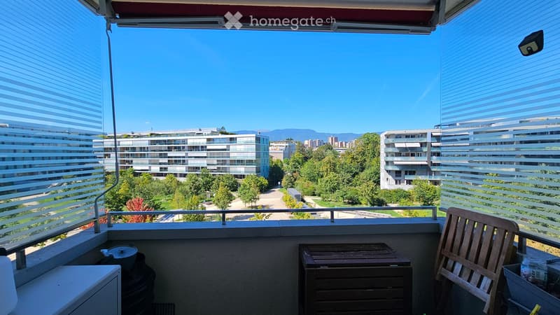 Balcony with wooden chair and table, overlooking a cityscape with modern buildings and greenery.